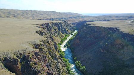 A blue river runs along the canyon. Green grass and trees. Boiling river in the canyon. Around the desert. View of the road. Steep edges of the canyon.の写真素材