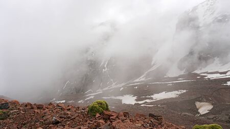 Large clouds swim through the gorge. Mountainous area. Snow is visible on the mountain slopes. Green moss grows on the stones. Hiking in the mountains. Snowy peak.の写真素材