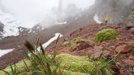 Large clouds swim through the gorge. A group of climbers climbs the peak. On the shoulders of large backpacks. Snow is visible on the mountain slopes. Green moss grows on the stones. Mountainous area.の写真素材