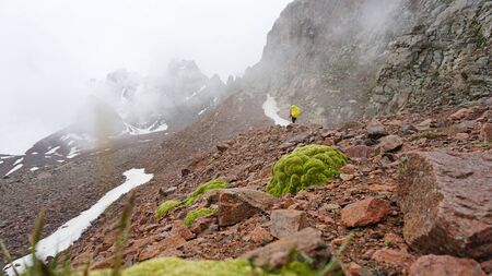 Large clouds swim through the gorge. A group of climbers climbs the peak. On the shoulders of large backpacks. Snow is visible on the mountain slopes. Green moss grows on the stones. Mountainous area.の写真素材