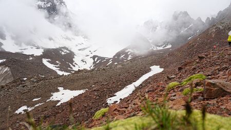 Large clouds swim through the gorge. A group of climbers climbs the peak. On the shoulders of large backpacks. Snow is visible on the mountain slopes. Green moss grows on the stones. Mountainous area.の写真素材