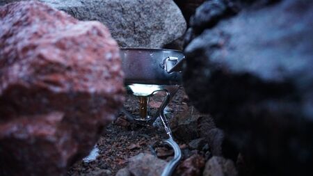 The process of cooking on the burner. Portable stove among the stones. The fire is burning. Works from gas. Melting the snow. Convenient device for a hike and a small pot.の写真素材