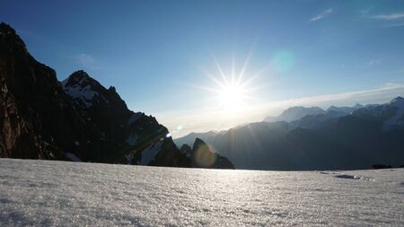 The sun shines brightly. View of snowy mountains, blue sky, cliff and white clouds. The rays are reflected from the snow. Panarama of the mountains.の写真素材