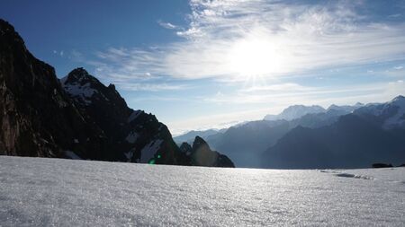 The sun shines brightly. View of snowy mountains, blue sky, cliff and white clouds. The rays are reflected from the snow. Panarama of the mountains.の写真素材