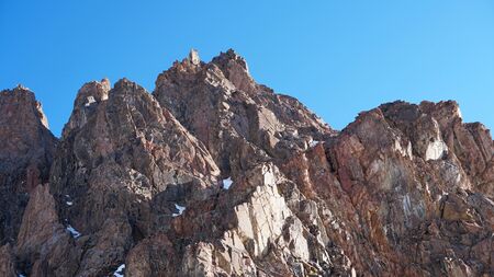 Rocky mountain top. You can see little people. Climbers climb to the top. Large rocks on the sides. Sometimes there is snow. Blue clear sky.の写真素材