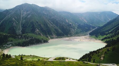 Big Almaty lake located in the mountains of Kazakhstan. It offers views of green grass, flowers, lake, rocks, large mountains and the sky in the clouds. Mountain lake with blue water.の写真素材