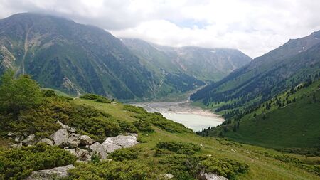 Big Almaty lake located in the mountains of Kazakhstan. It offers views of green grass, flowers, lake, rocks, large mountains and the sky in the clouds. Mountain lake with blue water.の写真素材