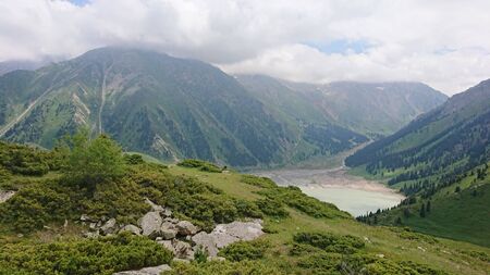 Big Almaty lake located in the mountains of Kazakhstan. It offers views of green grass, flowers, lake, rocks, large mountains and the sky in the clouds. Mountain lake with blue water.の写真素材