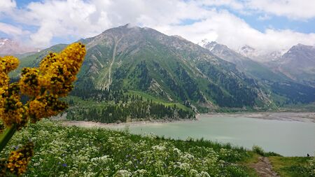 Big Almaty lake located in the mountains of Kazakhstan. It offers views of green grass, flowers, lake, rocks, large mountains and the sky in the clouds. Mountain lake with blue water.の写真素材