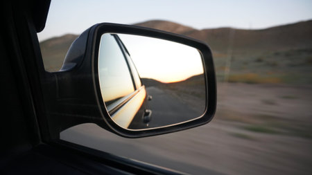 View in the side mirror of the car. Orange dawn beyond the hills. The car goes at speed. Visible...