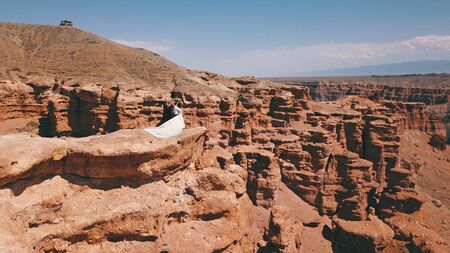 Charyn canyon and a young couple. A girl in a white dress, a guy in a shirt and jeans. Landscape as if on Mars. Big cracks, red rock, blue sky with clouds. In the distance you can see the hills.の写真素材