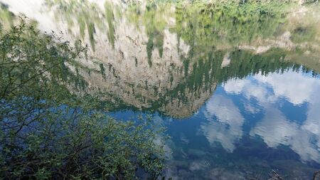Kolsay lake located in the mountains of Kazakhstan. Turquoise water as a mirror. The water reflects the mountains, green hills, tall spruce, grass, sky and clouds. Beautiful landscape of mountain lake.の写真素材