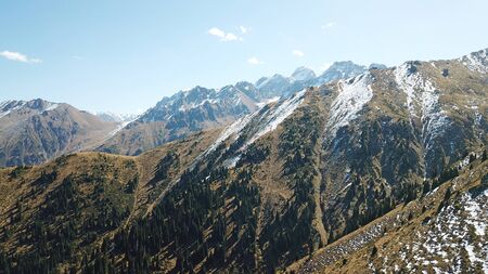 Autumn in the mountains. Green-orange wood, the grasses, coniferous ate. Big rocks and snow-capped mountains. Mountain gorge. Yellow bushes and grass. Shooting from a height, drone. Almaty, Kazakhstan.の写真素材
