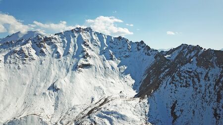 Snow-capped mountains. White clouds and blue sky. Autumn in the mountains, but already lies snow. Height 4000 m. Large stones lie on the slopes. Kazakhstan, TRANS-Ili Alatau, Almaty.の写真素材