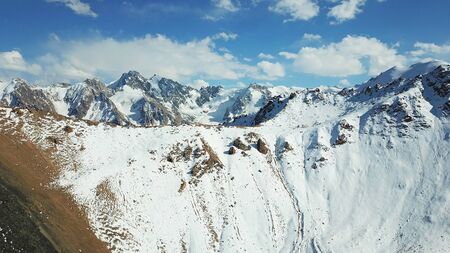 Snow-capped mountains. White clouds and blue sky. Autumn in the mountains, but already lies snow. Height 4000 m. Large stones lie on the slopes. Kazakhstan, TRANS-Ili Alatau, Almaty.の写真素材