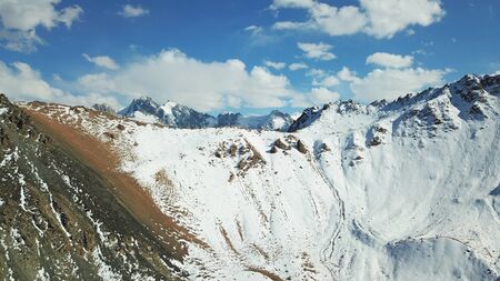 Snow-capped mountains. White clouds and blue sky. Autumn in the mountains, but already lies snow. Height 4000 m. Large stones lie on the slopes. Kazakhstan, TRANS-Ili Alatau, Almaty.の写真素材