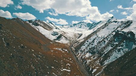 Autumn in the mountains. Yellow grass and snow-capped mountains. The gorge with the river. Blue sky and big white clouds. The stones lie on the slopes, in some places the snow. Almaty, Kazakhstan.の写真素材