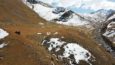 Autumn in the mountains. Yellow grass and snow-capped mountains. The gorge with the river. Blue sky and big white clouds. The stones lie on the slopes, in some places the snow. Almaty, Kazakhstan.の写真素材