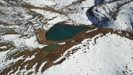 Mountain lake among the snowy peaks. Moraine lake Titova, in the mountains of Almaty, Kazakhstan. Height 3377 m. Shooting with a drone. Yellow rocks, white clouds, snow and blue sky. Highest peak.の写真素材