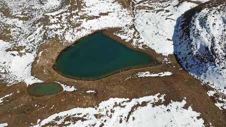 Mountain lake among the snowy peaks. Moraine lake Titova, in the mountains of Almaty, Kazakhstan. Height 3377 m. Shooting with a drone. Yellow rocks, white clouds, snow and blue sky. Highest peak.の写真素材