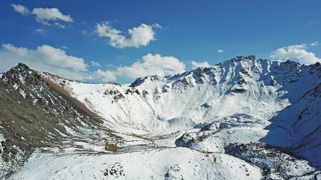 Mountain lake among the snowy peaks. Moraine lake Titova, in the mountains of Almaty, Kazakhstan. Height 3377 m. Shooting with a drone. Yellow rocks, white clouds, snow and blue sky. Highest peak.の写真素材