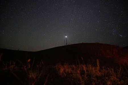The bright starlight of the night sky. The milky way, meteorites and nebula are visible. The stars illuminate the ground, the grass and the post. Night landscape of the starry sky.の写真素材
