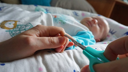 A newborn childs nails are cut with special baby scissors. An adult hand holds a small childs hand. Carefully, the mother cuts her daughters nails. A child in a cocoon, home environment. Trust.の写真素材