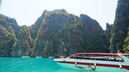 Blue water, green hills and steep rocks. The boat sails near the island. Boat with tourists in the Bay. Steep cliffs and caves. Group of tourists on the boat. Sea excursion. Water gradient.の写真素材
