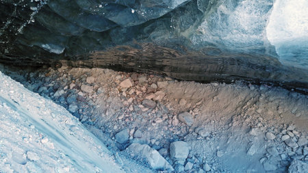 Ice cave in the snowy mountains. Tuyuk-Su glacier. Black ice reflects everything like a mirror. The ledge of stones collapsed. huge cracks in the ice tunnel. Snowy mountains of Almaty, Kazakhstan.の写真素材