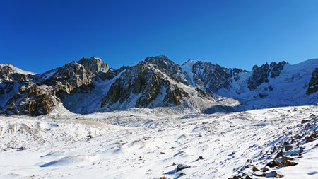 High rocks covered with snow. The Tuyuk Su Glacier. The view from the drone to the tops of the peaks. Completely surrounded by winter mountains. blue clear sky and bright sun. Shadows from mountainsの写真素材