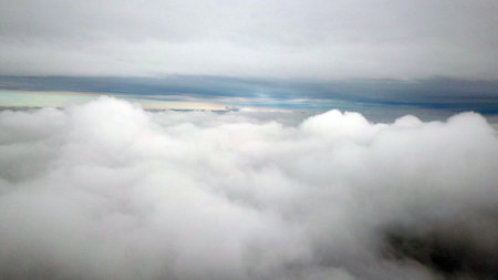 Top view through the clouds on the city of Almaty. Winter atmosphere, white trees, bushes, roofs of houses. Flying over the city. White clouds and light fog. Traffic of cars on roads. Through clouds.の写真素材