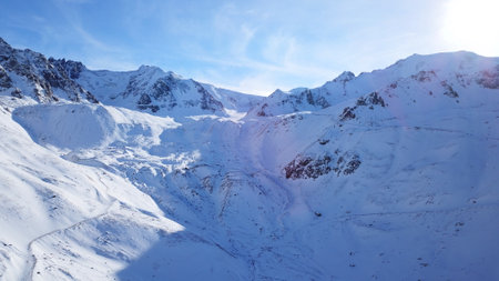 Snow mountain peaks with rocks. View from drone. In places, you can see glaciers, large rocks and rocks. Huge drifts of snow covered mountains. Dangerous place. Blue sky and sun. Shadow of the peaks.の写真素材