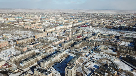 A small town on the shore of lake Balkhash. Top view of houses, cultural buildings, snowy streets, gray roads with cars and a green lake. The lake is partially covered with ice. Soviet city.の写真素材