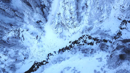 A majestic snowy gorge with fir trees in mountains. Tall trees brush against white clouds. Steep cliffs with large rocks are covered with snow. Top view from the drone. Almarasan, Almaty, Kazakhstanの写真素材