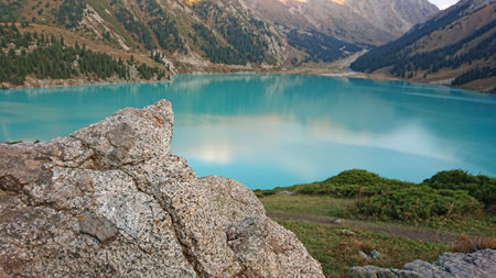 Big Almaty lake in the mountains. Green hills, flowers and fields. White clouds over the mountains. Mountain lake. In places there are stones. Protected place of nature, reserve of TRANS-ili Alatauの写真素材