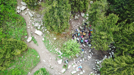 A group of people stopped for a rest in the forest. Top view from a drone. Tourists are having a picnic. Grass all around, tall firs, and a trail nearby. Lots of big rocks. In the center of the fire.の写真素材