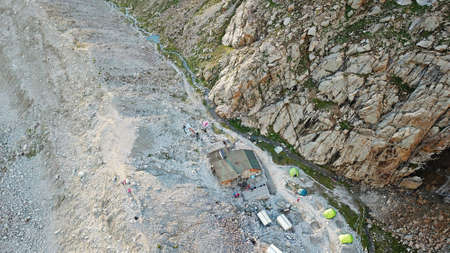 Camping high in the mountains. Rocky terrain. There are tents, climbers are resting. Next to it is a built house with solar panels, a river runs, and a green tarva runs along the edges. Top view.の写真素材