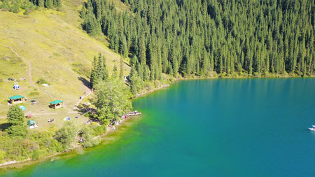 Kolsay lake among green hills and mountains. The mountain lake is surrounded by green forest, tall coniferous trees, grass and bushes. Clean water is like a mirror. Tourists swim on boats. Kazakhstanの写真素材