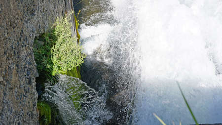 Draining the water pressure into the river. The water flows like a waterfall and flows into the river. There are concrete walls around the edges, and iron pipes are visible. Trees grow in the distanceの写真素材