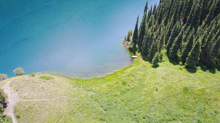 Kolsay lake among green hills and mountains. The mountain lake is surrounded by green forest, tall coniferous trees, grass and bushes. Clean water is like a mirror. Tourists swim on boats. Kazakhstanの写真素材
