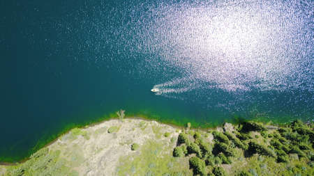 Kolsay lake among green hills and mountains. The mountain lake is surrounded by green forest, tall coniferous trees, grass and bushes. Clean water is like a mirror. Tourists swim on boats. Kazakhstanの写真素材
