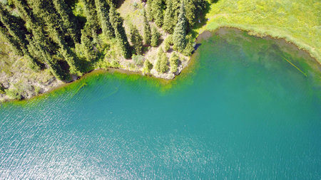 Kolsay lake among green hills and mountains. The mountain lake is surrounded by green forest, tall coniferous trees, grass and bushes. Clean water is like a mirror. Tourists swim on boats. Kazakhstanの写真素材