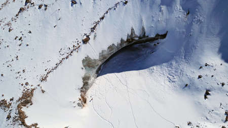 A huge wall of ice. Bogdanovich Glacier in the mountains of Almaty. The wind blows the snow away from the high frozen wave. Unusual shape and color of the ice. Moraine lake in winter in the mountainsの写真素材