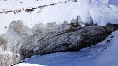 A huge wall of ice. Bogdanovich Glacier in the mountains of Almaty. The wind blows the snow away from the high frozen wave. Unusual shape and color of the ice. Moraine lake in winter in the mountainsの写真素材