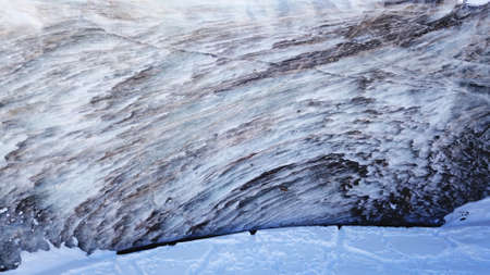 A huge wall of ice. Bogdanovich Glacier in the mountains of Almaty. The wind blows the snow away from the high frozen wave. Unusual shape and color of the ice. Moraine lake in winter in the mountainsの写真素材