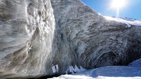 High ice wall in the mountains. The Bogdanovich Glacier. The black-and-white ice mixed. Grains of...