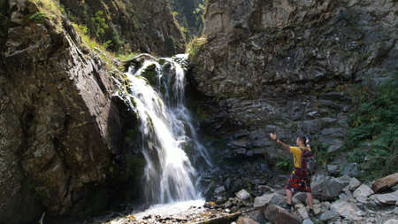 A guy with a backpack is standing near a waterfallの写真素材