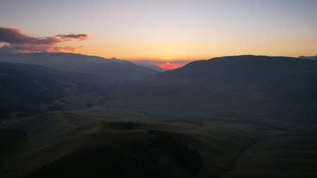 Red rays of the sun at sunset among the mountainsの写真素材