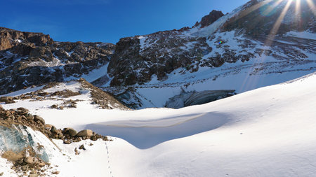 Snowy high mountains with bright sun and rocks.の写真素材