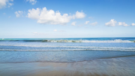 Golden sand and blue ocean water with white cloudsの写真素材